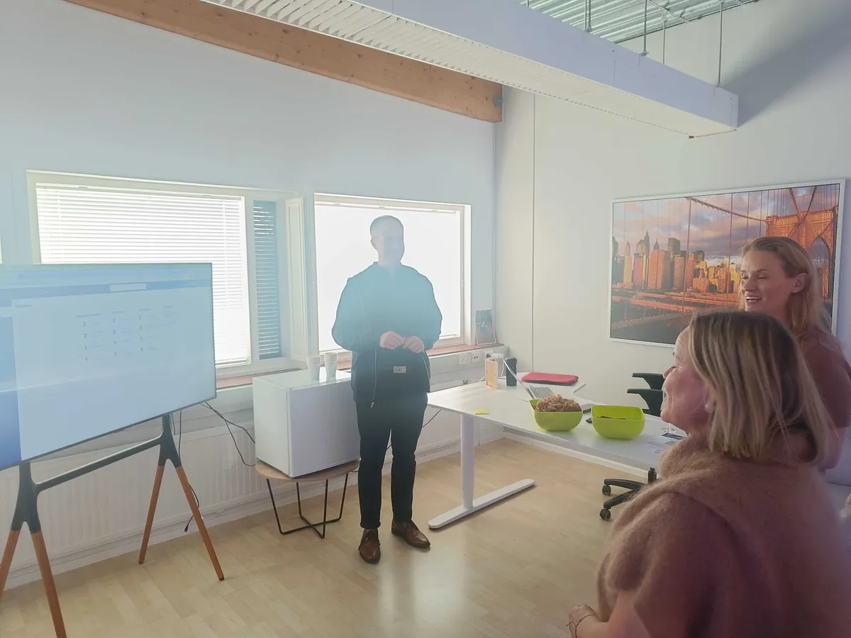Jaakko presenterar handlarpanelen på en stor skärm för två lyssnande gäster i utvecklingsteamets rum.