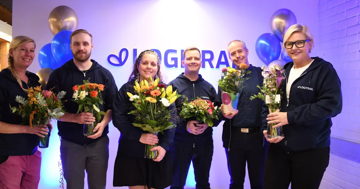 Logitrails team ler med blombuketter i händerna framför den upplysta Logitrail-väggen, omgivna av ballonger.