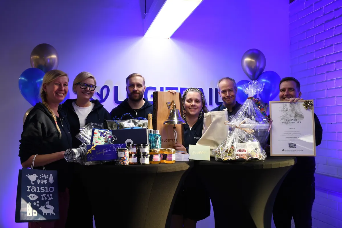 Sex medlemmar ur Logitrails ledningsgrupp ler bakom ett bord fullt av gåvor, bland annat skeppsklockan och det inramade gåvobeviset för gammal skog.