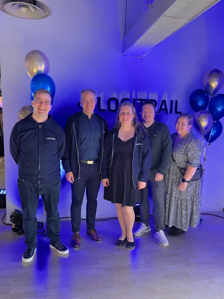 Logitrails fem grundare ler tillsammans framför Logitrail-väggen, omgivna av ballonger.